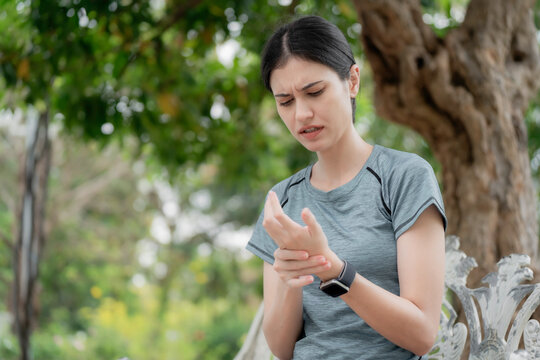 Young woman feeling numbness and tingling in fingers after outdoor workout in park, holding painful wrist, nerve pain and neuropathy health concept. numbness, tingling, fingers, nerve, neuropathy.