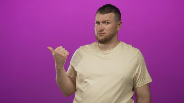 Man pointing thumb to the side in purple studio wearing beige tshirt with scowling face and scrunched nose; skepticism.