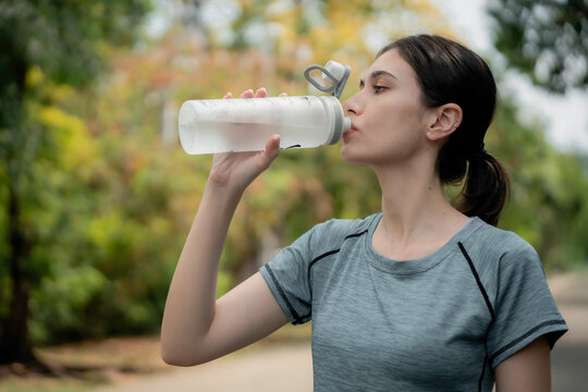 Young woman runner holding water bottle in park after jogging, smiling and staying hydrated during outdoor workout, healthy lifestyle and fitness concept. woman, runner, water, bottle, park, jogging.