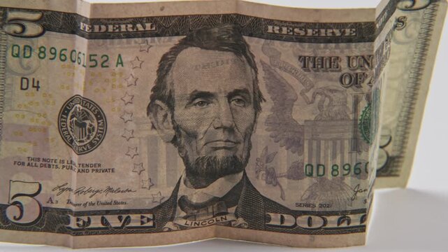 Close up of Abe Abraham Lincoln face on five 5 dollar cash paper bill in detail slo mo slow motion on green white text texture of American economy paperback financial bills of multiple dollars symbol