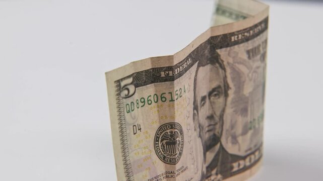 Close up of Abe Abraham Lincoln face on five 5 dollar cash paper bill in detail slo mo slow motion on green white text texture of American economy paperback financial bills of multiple dollars symbol