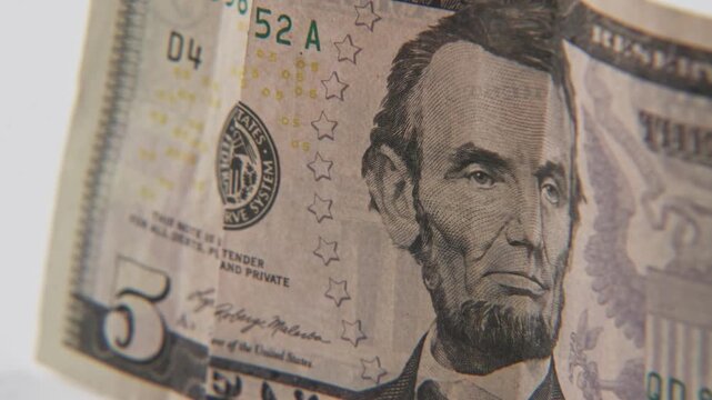 Close up of Abe Abraham Lincoln face on five 5 dollar cash paper bill in detail slo mo slow motion on green white text texture of American economy paperback financial bills of multiple dollars symbol