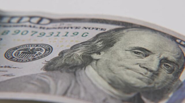 Close up slow motion of Ben Franklin face on American United States of America one hundred 100 dollar bill printed paper texture on high value paper currency in macro studio lighting in tight detail