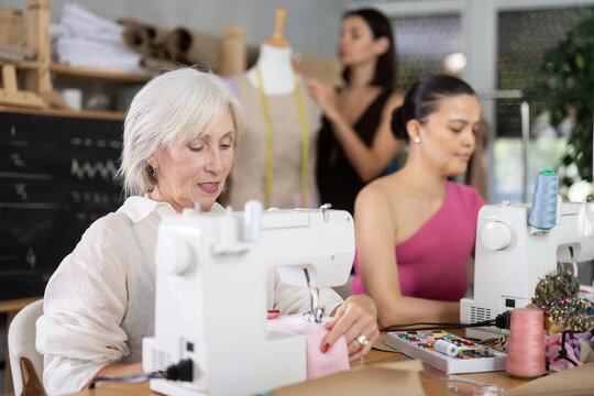 Group of women sewing on machine and working with mannequin during lesson at sewing workshop