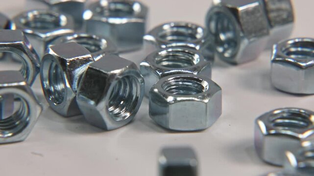 Slow motion close up of screw bolt imperial metric nuts that are silver, steel, and metal falling into place on white surface for industrial work in a tech technology electronics shop studio lighting