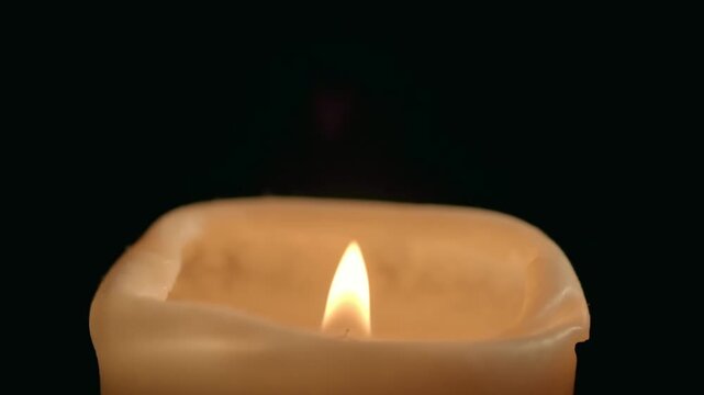 Close up slow motion video of a candle flame being blown out and extinguishing against a black background.