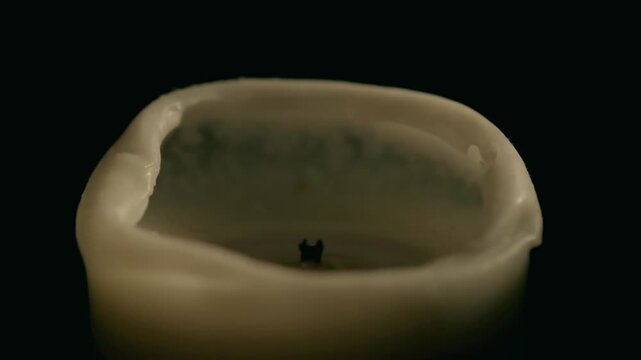 Close up slow motion video of a match striking and lighting a candle wick against a pure black background.