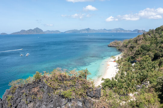 Wide aerial view of Seven Commandos Beach with palm forest, boats and clear blue tropical sky