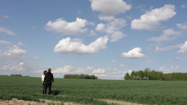 a loving couple walking through a field in summer