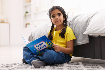 Fototapeta premium Cute little girl reading book on floor at home