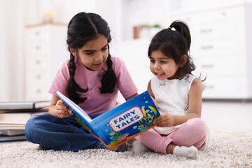 Fototapeta premium Cute little girls reading book together at home