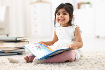 Fototapeta premium Cute little girl reading book on floor at home. Space for text