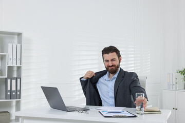 Man with glass of water suffering from heat at table near white wall indoors, space for text