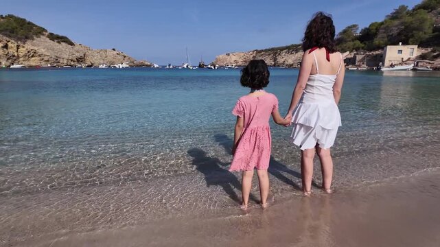 Mother and Daughter Standing by Turquoise Beach, Facing the Sea