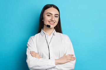 Portrait of smiling hotline operator in headset with crossed arms on light blue background