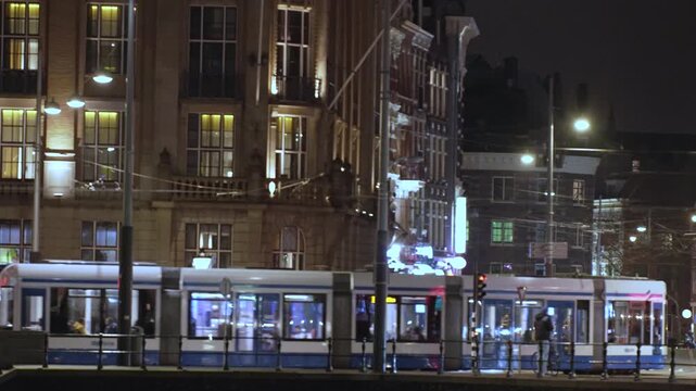 Amsterdam Tram Passing Historic Buildings at Night Near Central Station