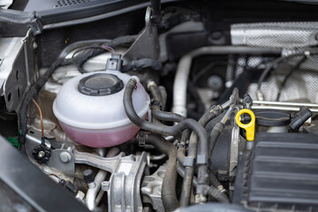 Fototapeta premium Close up of a modern car engine bay featuring pink coolant expansion tank and yellow oil dipstick. Vehicle maintenance, automotive engineering and technical liquid checkup details