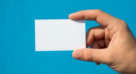 Obraz premium Hand holding blank white business card on bright blue background for branding and corporate identity mockup design projects.