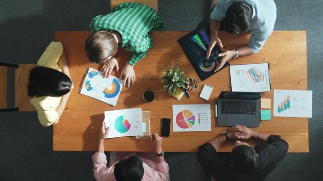 Top view of project manager using tablet to analyze data and financial chart while marketing team working together to brainstorm marketing campaign or planning strategy at meeting room. Convocation.