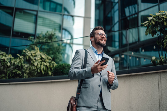 Happy businessman using smartphone and wireless earbuds