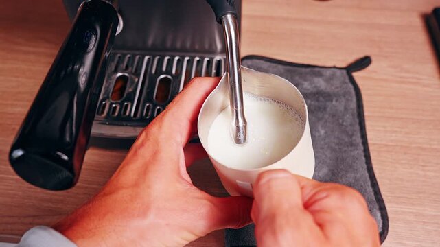 Top Down View of Barista Holding Metal Milk Pitcher Under Steam Wand While Heating Milk Showing Control of Temperature and Creamy Texture During Coffee Preparation