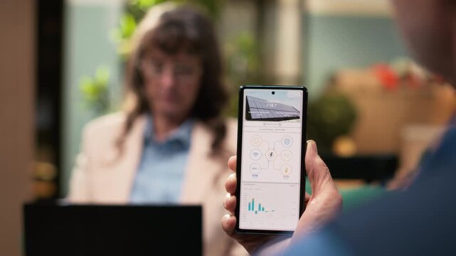 Aged man and woman reviewing green energy system through software on mobile phone. Sustainable, eco and clean power solutions like photovoltaic panels and off-grid solar energy at home.