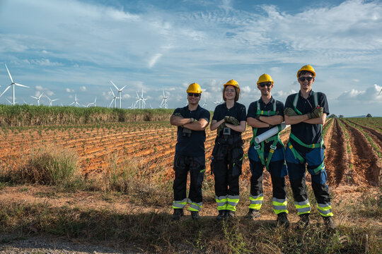 Industrial HSE safety supervisors and engineering workforce wearing full fall protection PPE posing at wind farm site. Professional team adhering to occupational health standards.