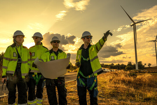 Industrial HSE safety supervisors adhering to strict occupational ppe regulations at sunset. Diverse engineering workforce surveying power generation site.