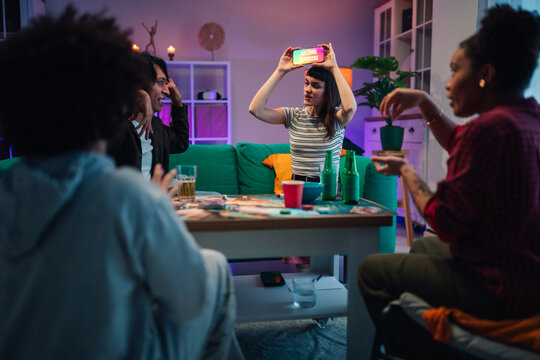 Diverse friends playing charades with a smartphone at a cozy home party, enjoying fun leisure time together