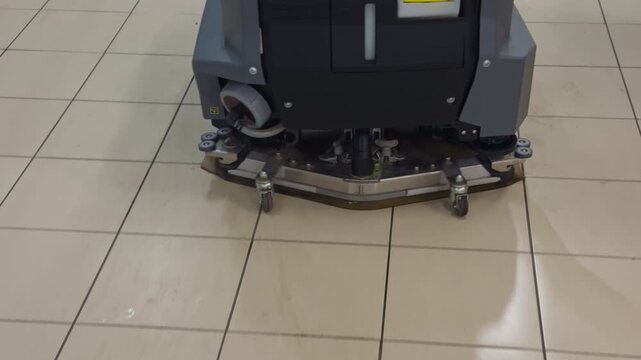 Cleaning supermarket tiles with rotating brushes. Detailed view of floor scrubbing machine cleaning supermarket tiles in daylight
