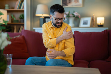 Obraz premium Young man experiencing shoulder pain at home