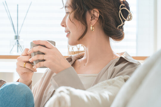 リビングのソファーに座りホットドリンクを飲むオシャレな女性
