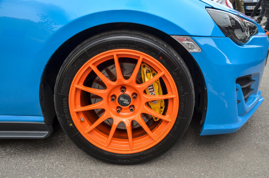 Front wheel of a Subaru BRZ sports coupe in blue with bright orange multi-spoke rim and yellow brake calipers
