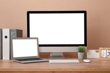 Fototapeta premium Modern laptop, computer monitor, folders and calendar on table near color wall