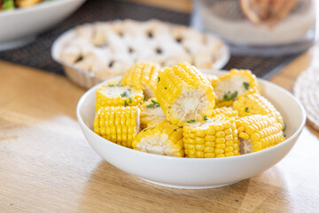 White ceramic bowl holding buttered corn rounds with chopped parsley on light wooden dining table