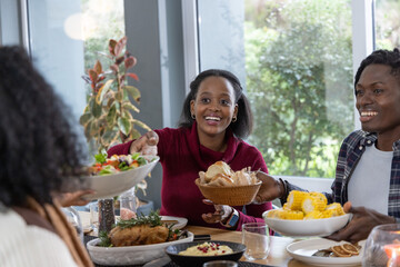 African American friends passing dishes at home, woman in burgundy knit holding woven bread basket