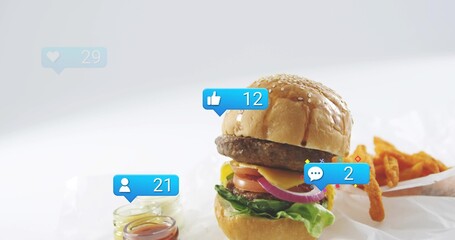 Showcasing stacked cheeseburger on white paper at studio, with fries, glass jars, reaction badges