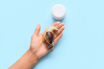 Female hand with snail and jar of cream on blue background © Pixel-Shot