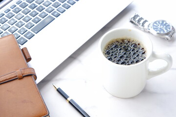 淹れたての美味しいコーヒーを飲みながら、ノートパソコンとシステム手帳でデスクワークをしているイメージ
