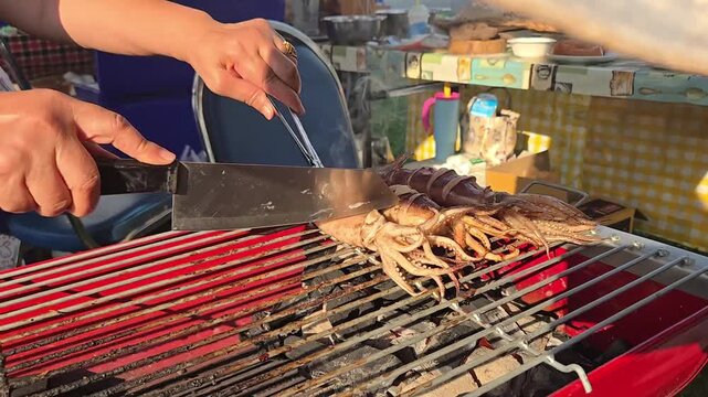 Vendor cut Grilled fresh whole squids on charcoal grill. Traditional thai street food at market. Close up