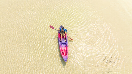 Aerial top view of a young woman paddling a yellow kayak in crystal clear turquoise sea water near white sand beach. Tropical summer vacation and water sports and summer vacation concept.	
