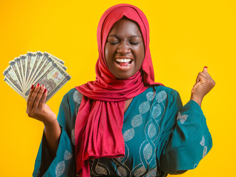 An ecstatic woman in a red hijab and teal dress celebrates a financial windfall, holding a fan of Eritrean banknotes against a bright yellow backdrop in a vivid display of success and pure happiness.
