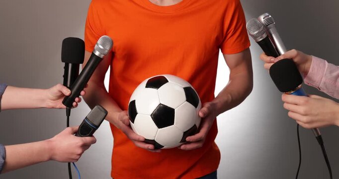 Sportsman with soccer ball giving interview to journalists on grey gradient background, closeup