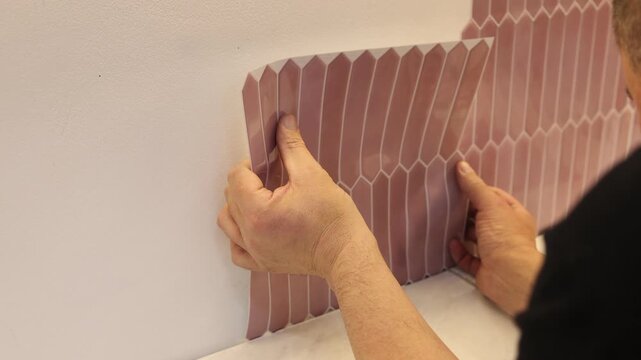 Man applying peel and stick tiles on wall in kitchen, closeup