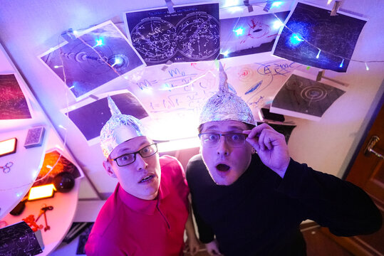 Two men in tinfoil hats observing an invisible phenomenon, illuminated by neon purple lights and diagrams on the walls, create a dramatic atmosphere, UFO, ufologists