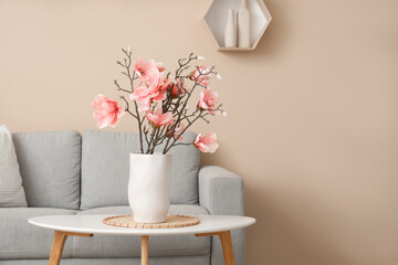 Cozy sofa and magnolia flowers in vase on coffee table in interior of living room © Pixel-Shot