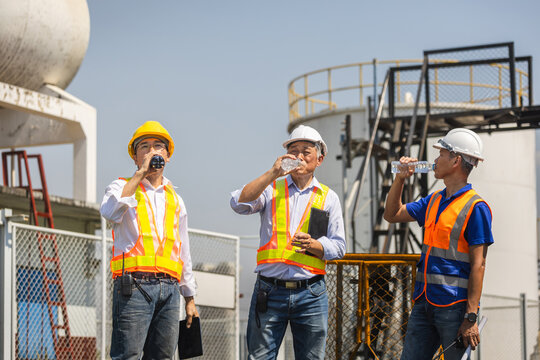 Group of diverse engineers drinking bottled water to stay hydrated at industrial site, Senior and young engineers taking a refreshing water break during sunny outdoor shift