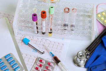 Test tubes with blood samples sit on lab table beside medical tools, heart chart papers, pills.