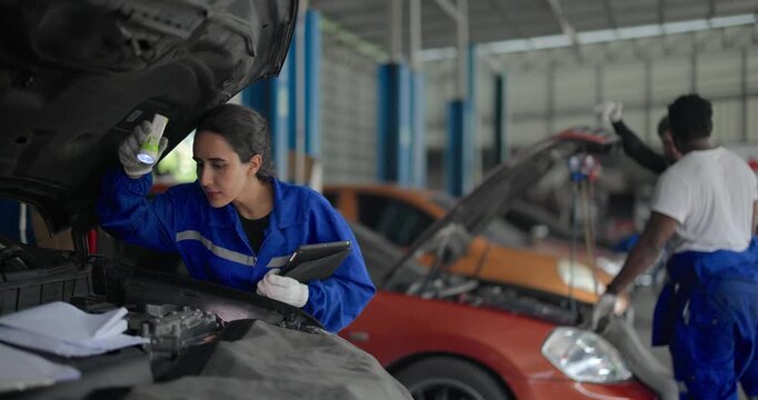 Mechanic use vehicle's onboard diagnostic tool to identify error codes in automotive workshop. Focusing intently on tablet device, showcasing modern diagnostic techniques and technical expertise.
