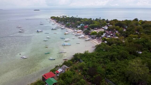 GILUTONGAN ISLAND, CEBU, PHILIPPINES - MARCH 24, 2020: Aerial drone view of the long wooden pier and outrigger boats on the turquoise coral reef waters of Hilutungan Island